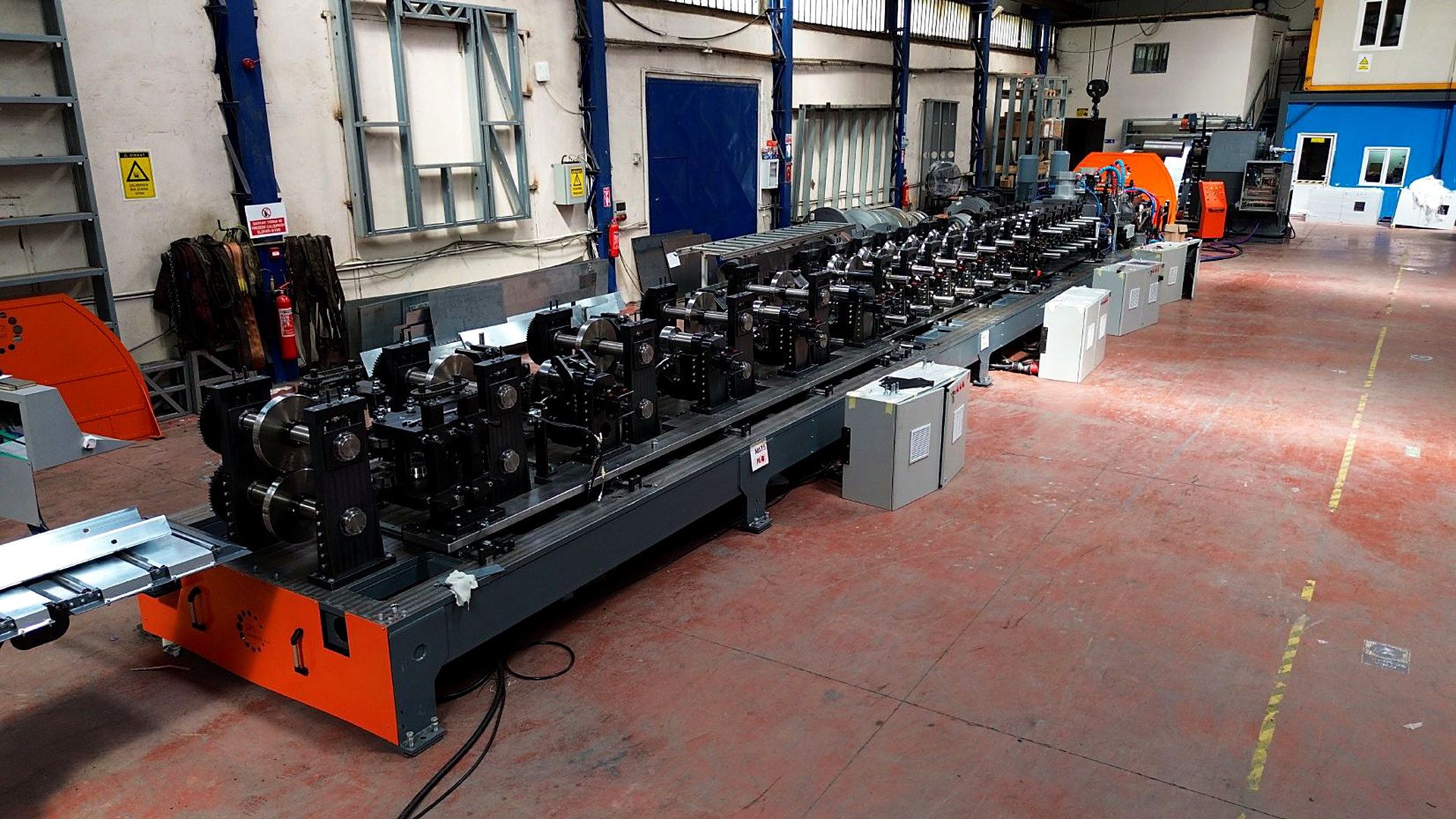 Automated purlin roll-forming line in a factory hall, seen from the infeed end
